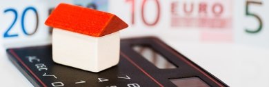 Haus aus Bauklötzen auf einem Taschenrechner und im HIntergrund sind Euronoten zu sehen